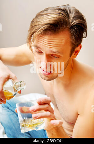 Ubriaco uomo seduto sul letto e di bere whisky Foto Stock
