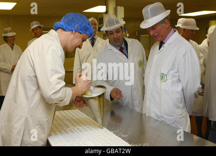 Andy Joslin (centro), direttore dello stabilimento, chiede al Principe del Galles se desidera provare a pompare in modo fondente durante una visita alla fabbrica di cioccolato Dorchester di Poundbury, Dorset. Il principe si scusò con Kevin Greening (a sinistra) per "fare un pasticcio di esso". Foto Stock