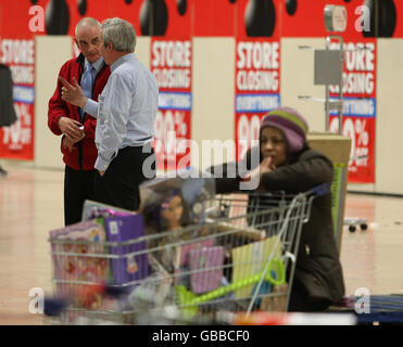 Un acquirente con un trolley imballato prende una pausa durante l'ultimo giorno di negoziazione presso il negozio Woolworths a Edimburgo, mentre i membri del personale parlano in background. Foto Stock