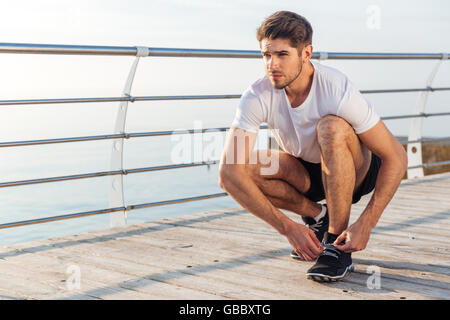 Primo piano dell'uomo atleta lacci il suo sneakers sul molo Foto Stock