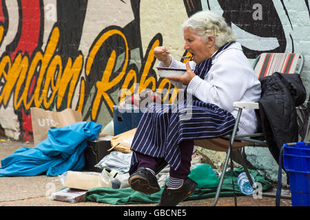 Donna anziana seduto a pranzo al mercato da Brick Lane Shoreditch zona, Londra UK nel mese di luglio Foto Stock