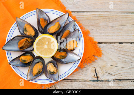 Le cozze al vapore su un tavolo in legno e una tovaglia arancione. spazio copia Foto Stock