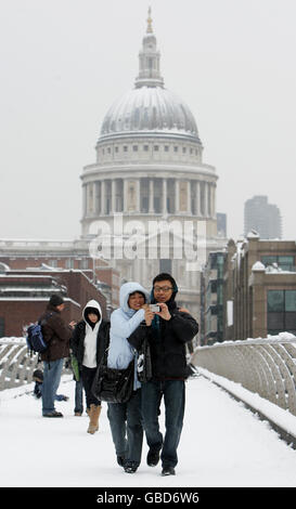 I pedoni attraversano il Millennium Bridge sul fiume Tamigi con la cattedrale di St Paul sullo sfondo mentre la neve continua a cadere nel centro di Londra. Foto Stock