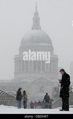 I pedoni attraversano il Millennium Bridge sul fiume Tamigi con la cattedrale di St Paul sullo sfondo mentre la neve continua a cadere nel centro di Londra. Foto Stock