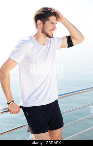 Bello sorridente giovane atleta in appoggio al molo dopo allenamento Foto Stock