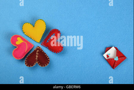 Sentivo artigianato e arte, quattro coloratissimi cucito a mano giocattolo cuori, rosso, rosa, giallo, marrone e busta su sfondo blu Foto Stock