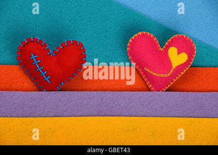 Artigianato e arte, due cucito a mano giocattolo Cuori rosa e rosso sul feltro colorato sfondo strisce Foto Stock