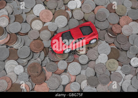 Motoring / auto costa concetto. Piccolo giocattolo auto sulla sommità di una pila di diffusione in modo casuale le monete del Regno Unito come una metafora per il bollo auto, auto in esecuzione delle spese. Foto Stock