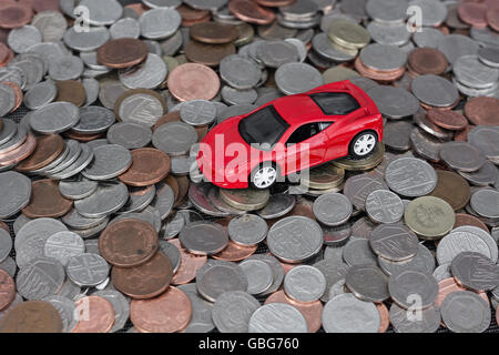 Motoring / auto costa concetto. Piccolo giocattolo auto sulla sommità di una pila di diffusione in modo casuale le monete del Regno Unito come una metafora per il bollo auto, auto in esecuzione delle spese. Foto Stock