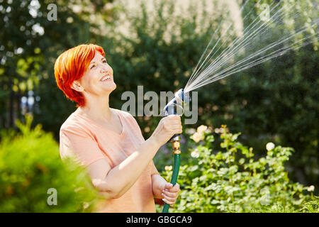 Senior donna innaffiando le sue piante nel suo giardino con cospargere Foto Stock