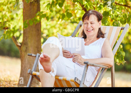 Rilassato donna senior di lettura su una sedia a sdraio in estate nel gardent Foto Stock