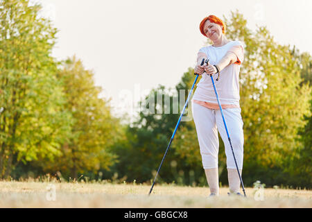 Felice donna senior camminare con bastoni nella natura e sorridente Foto Stock
