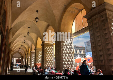 I turisti seduti presso il cafe le tabelle sotto il colonnato, accanto a Piazza Maggiore, Bologna, Italia Foto Stock