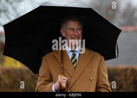 Il Principe del Galles si rifuga sotto un ombrello durante una visita alla sala del Villaggio di Aldford ad Aldford, Chester. Foto Stock