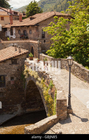 Donna che indossa un cappello di paglia sul ponte medievale di San Cayetano oltre il Fiume Deva nella città di Potes nel Parco Nazionale Picos de Europa Spagna Foto Stock