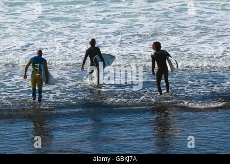 Tre surfisti maschio wading in acqua nella loro muta di fare surf a Sandon Point, Bulli, NSW, Australia. Foto Stock