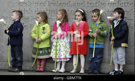 I bambini detengono un Lilly che rappresenta ciascuno dei leader giustiziati della Pasqua del 1916 durante la commemorazione annuale di Fianna Fail al cimitero di Arbour Hill a Dublino. Foto Stock