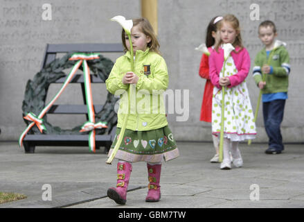 I bambini detengono un Lilly che rappresenta ciascuno dei leader giustiziati della Pasqua del 1916 durante la commemorazione annuale di Fianna Fail al cimitero di Arbour Hill a Dublino. Foto Stock