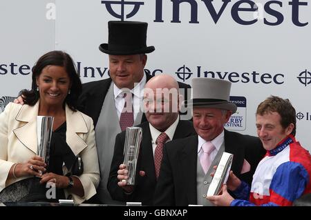 L'addestratore Dandy Nicholls (centro) Jockey Paul Quinn (a destra) festeggia con il loro trofeo dopo che l'itinerario indiano vince la corsa del 'trattino' di Investec durante il giorno di Derby all'ippodromo di Epsom Downs Foto Stock