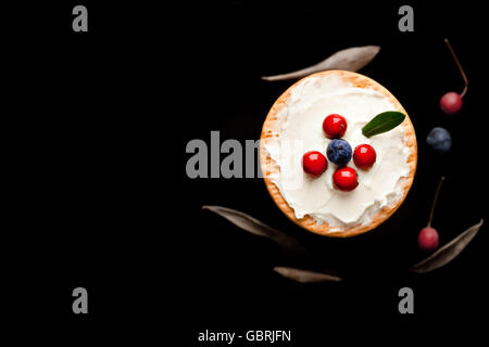 I biscotti con crema di formaggio e mirtilli sulla parte superiore circondata con bacche e foglie secche Foto Stock