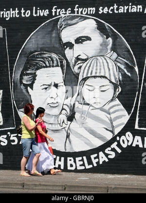 Due donne passano davanti a un murale dipinto di recente che fa riferimento ai recenti attacchi alle famiglie rumene sulla Falls Road a Belfast. Foto Stock