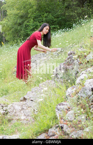 Ypung donna in fiore picking indossando abito rosso Foto Stock