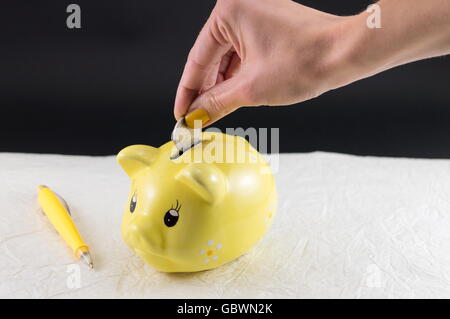 Donna mano inserire una moneta nel salvadanaio Foto Stock