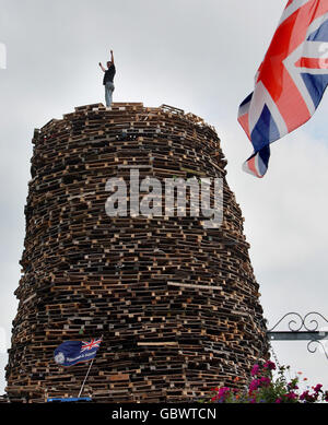 Un uomo si trova sulla cima di un falò a Newtownabbey, fuori Belfast. I falò si accenderanno in tutta l'Irlanda del Nord il 11 luglio o l'undicesima notte prima dei dodici festeggiamenti. Foto Stock