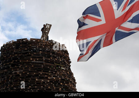 Un uomo si trova sulla cima di un falò a Newtownabbey, fuori Belfast. I falò si accenderanno in tutta l'Irlanda del Nord il 11 luglio o l'undicesima notte prima dei dodici festeggiamenti. Foto Stock