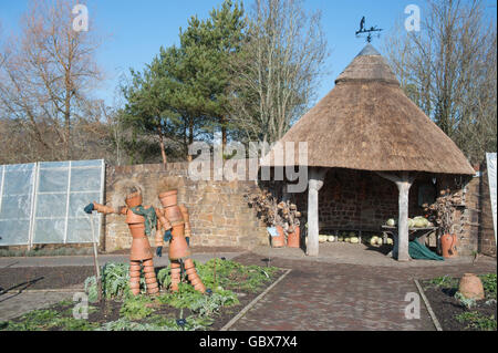 La terracotta Scarecrows nella parte anteriore del tetto di paglia Summer House in Orto in inverno al RHS Rosemoor, Devon Foto Stock