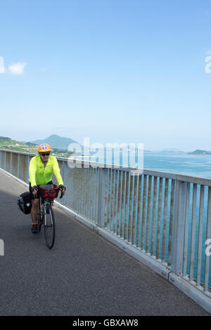 Una touring ciclista pedalare attraverso la Tatara ponte di collegamento tra le isole di Omishima e Ikuchi in Seto Inland Sea. Foto Stock