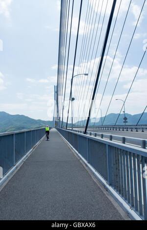 Un ciclista in bicicletta sulla pista ciclabile su theTatara ponte di collegamento tra le isole di Omishima e Ikuchi in Seto Inland Sea. Foto Stock