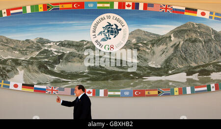 Il primo ministro italiano Silvio Berlusconi lascia la scena in cui i leader dei Paesi G8 e dei Paesi G5 sono destinati a proporre una 'foto di famiglia' nella seconda giornata del vertice G8 a l'Aquila, Italia. Foto Stock