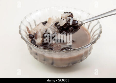 Dolce di riso appiccicoso e i fagioli neri in latte di cocco. Thai dessert su sfondo bianco. Foto Stock