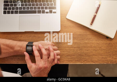 Vista superiore colpo di uomo seduto al suo posto di lavoro controllo tempo sul suo smartwatch. Imprenditore guardando il suo orologio. Focus su smart Foto Stock