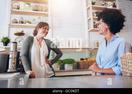 Due giovani donne a parlare e a sorridere mentre si lavora al banco bar. Felici i giovani lavoratori di sesso femminile in succo di frutta bar. Foto Stock