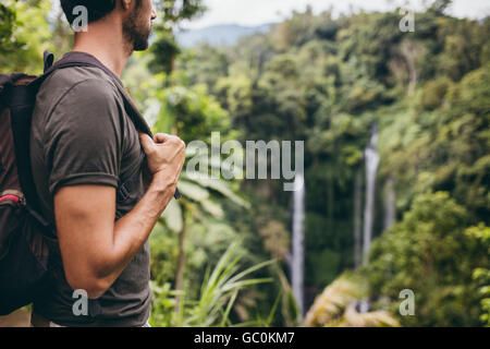 Immagine ravvicinata di giovane con zaino in piedi in natura e guardando a cascata. Escursionista maschio vicino a cascata nella foresta. Foto Stock