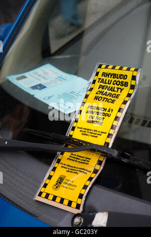 Un parcheggio auto penalità fissa avviso ticket, in gallese e lingua inglese, sul parabrezza di una vettura che ha anche un blue badge disabili Wales UK Foto Stock