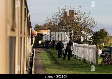 Una stazione di onde di guardia sul driver come passeggeri guarda dal treno a vapore carrello al Castello di Dunster stazione, Somerset REGNO UNITO Foto Stock