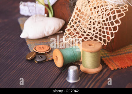 Rocchetto di filo, un ditale e una scatola con ricamo su una tavola di legno di close-up Foto Stock