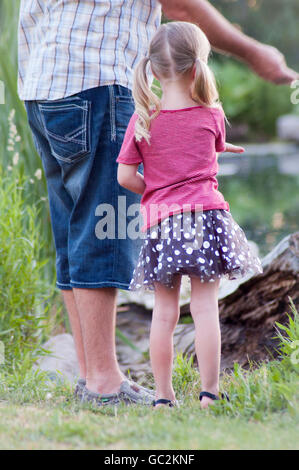 Bambina in piedi accanto al padre vicino laghetto dar da mangiare alle anatre Foto Stock