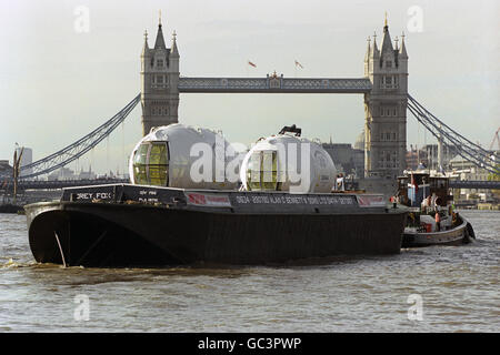 Le gondole che pendono dal London Eye, fanno il loro viaggio in barca lungo il Tamigi nel centro di Londra, arrivando al Tower Bridge, prima di andare sul sito della ruota gigante. Le 32 capsule possono impiegare fino a mezz'ora per viaggiare intorno alla ruota. Con un peso di 1.5 tonnellate e costruiti in Francia dalla compagnia di skilift Poma, le capsule offrono ai passeggeri una vista panoramica fino a 25 miglia di distanza. Foto Stock