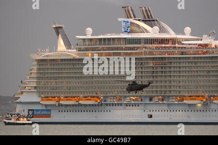 Un elicottero Royal Navy Sea King fa un volo lento passato della più recente e più grande nave da crociera del mondo, Oasis of the Seas, mentre entra nel Solent lungo il tragitto per Fort Lauderdale, Florida. Foto Stock