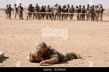 Un soldato dell'esercito britannico in un esercizio di addestramento alla ricerca di dispositivi esplosivi improvvisati (IED) a Camp Bastion in Afghanistan con i Marines americani in lontananza. Foto Stock