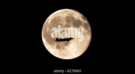 ALTERNATE CROP UN aereo passeggeri è silhouette contro la luna piena su Londra. Foto Stock