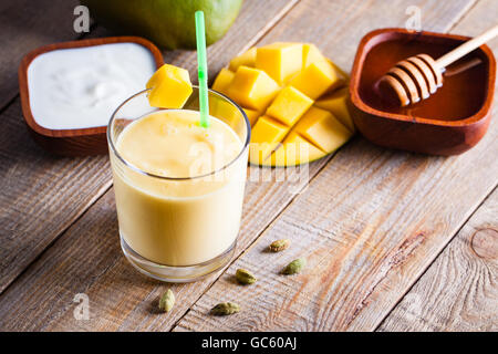 Bicchiere di mango lassi Indian bevanda aromatizzata con il cardamomo. Frullato su sfondo di legno. Foto Stock