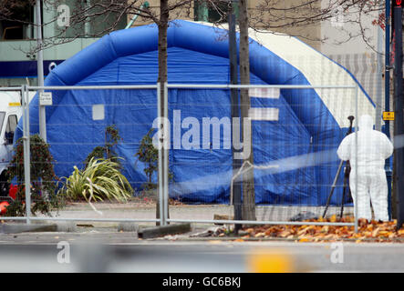 Gli ufficiali di polizia forense esaminano l'area intorno a un'auto che è parzialmente esplosa al di fuori del quartier generale del comitato di polizia a Belfast. L'auto, coperta da una tenda blu a scomparsa, conteneva una bomba da 400 libbre. Foto Stock