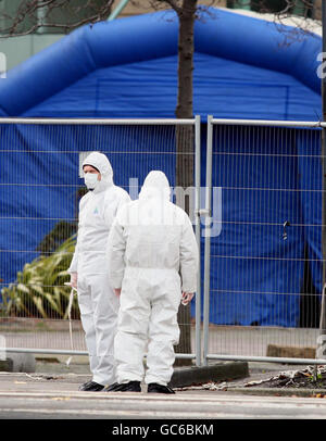 Gli ufficiali di polizia forense esaminano l'area intorno a un'auto che è parzialmente esplosa al di fuori del quartier generale del comitato di polizia a Belfast. L'auto, coperta da una tenda blu a scomparsa, conteneva una bomba da 400 libbre. Foto Stock