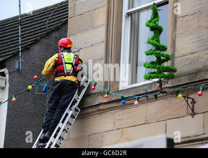 Un vigili del fuoco lavora sulle luci di Natale a Cockermouth High Street dopo che le acque alluvionali si sono recedite. Foto Stock