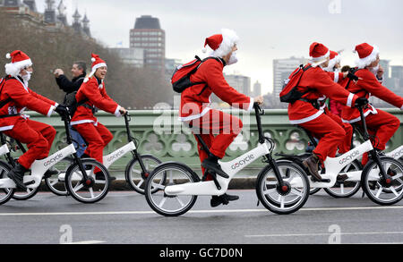 Le persone vestite come Santa on Gocycles attraversano il Westminster Bridge di Londra per promuovere la fibra di carbonio, elettrica, pieghevole bicicletta. Foto Stock